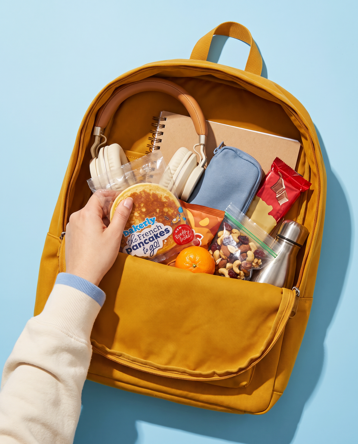 Hand packing bakerly pancakes into a yellow school backpack